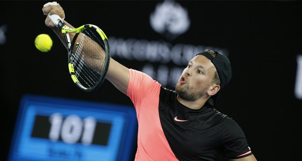 A man in a wheelchair wearing a pink and black Nike t-shirt hits a tennis ball