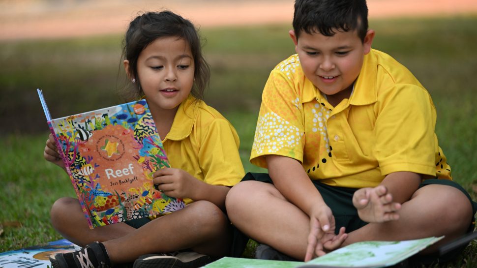 A young boy and girl sit and read a book outside. 