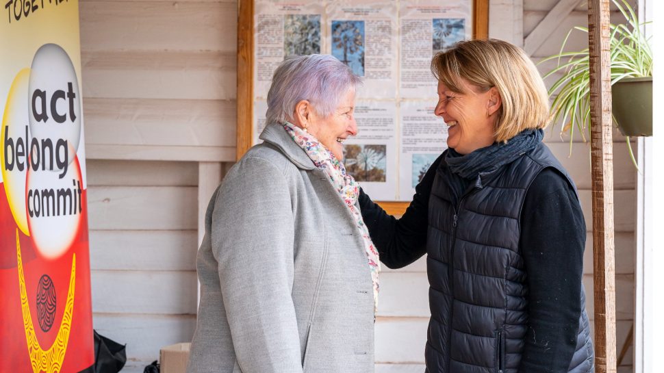 A middle-aged woman chatting with an elderly woman and placing her hand on her shoulder. 