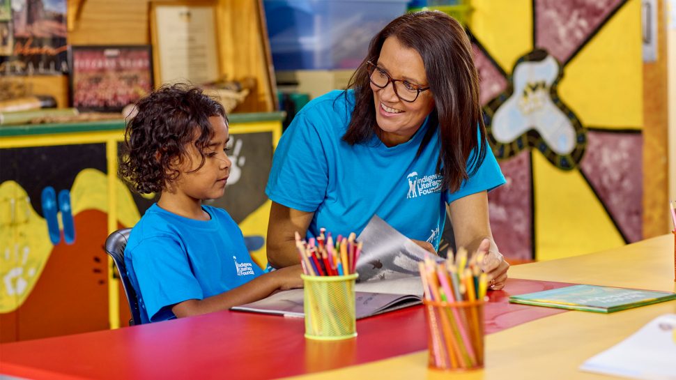 Indigenous author and teacher Shelley Ware is sitting with an Indigenous child in a classroom. 